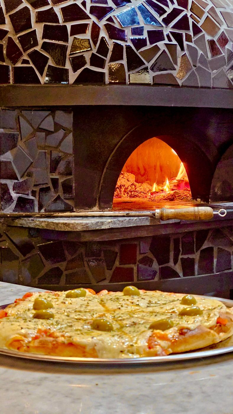 Muzzarella con aceitunas recién salida, frente al horno a leña de mosaico de Una Pizza