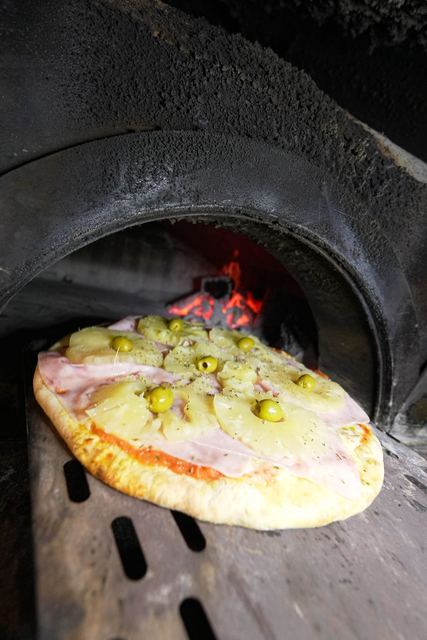 Pizza de ananá con jamón entrando al horno a leña