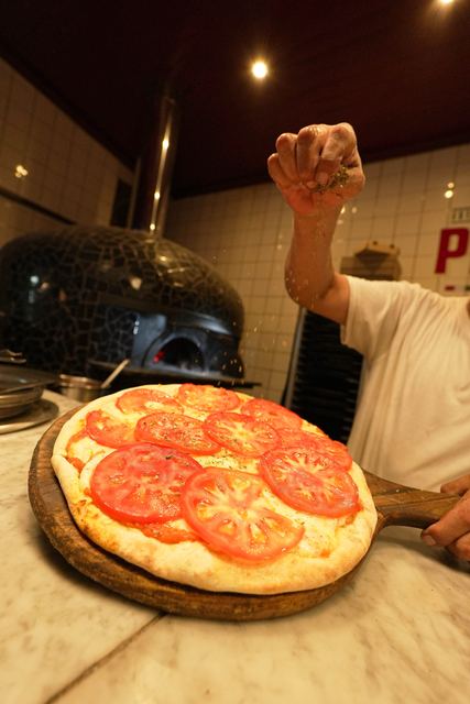 Pizzero de Una Pizza con una pizza de tomate recién armada, horno a leña atrás